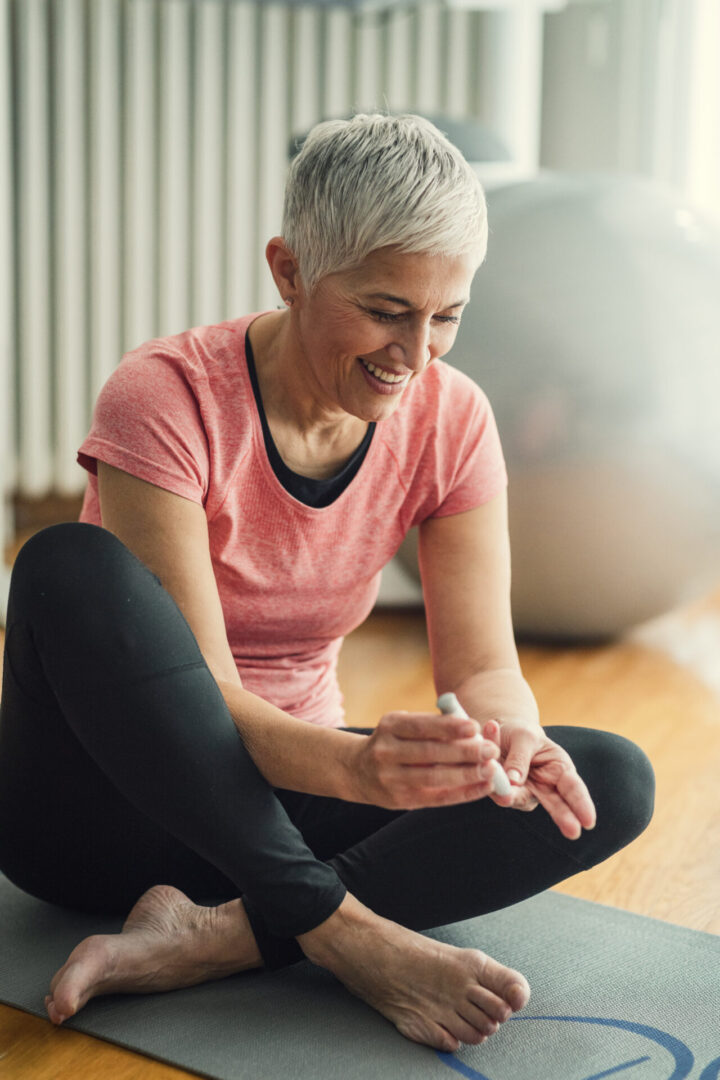 Mature woman doing blood sugar test at home in a living room. Selective focus to her hand.